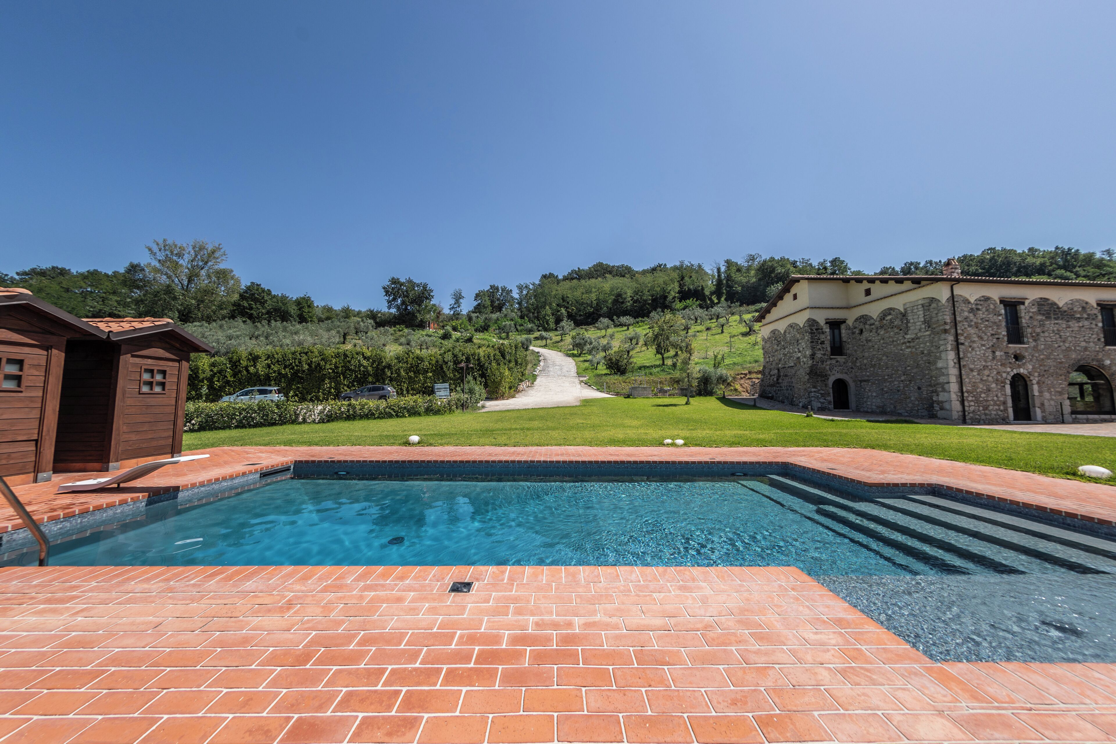 A swimming pool with a brick deck, surrounded by a grassy area and a stone building.