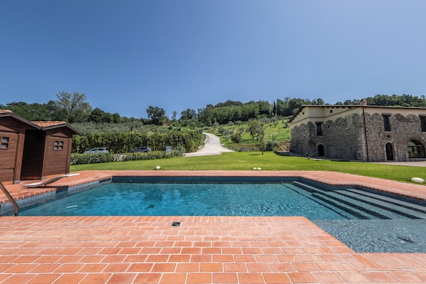 A swimming pool with a brick deck, surrounded by a grassy area and a stone building.
