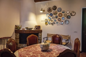A dining room with a fireplace, a wall of decorative plates, and a table with a floral tablecloth. - Dimora Santē – Historic Villa Surrounded by Olive Trees (Campania)