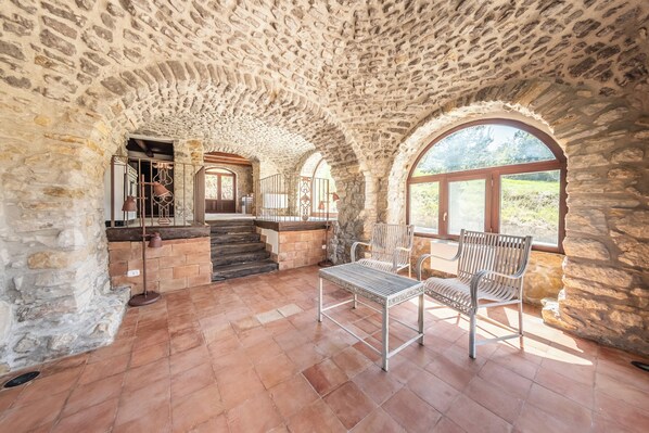 A stone-walled interior with a staircase leading to a door, two metal chairs, and a large window.