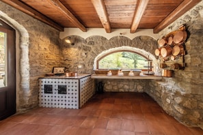 A rustic kitchen with stone walls, wooden beams, and a tiled floor. - Dimora Santē – Historic Villa Surrounded by Olive Trees (Campania)
