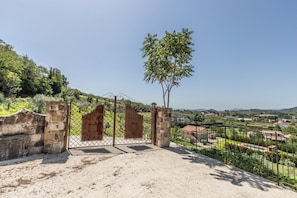 A gated entrance with a view of a rural landscape, including houses and hills.