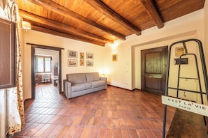 A room with a wooden ceiling, a grey sofa, tiled flooring, and a door with a sign reading 'C'EST LA VIE PARIS'.