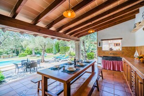 A covered outdoor dining area with a pool and lounge chairs in the background. - Rustic Country Retreat for 4 (Pollença)