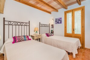 A bedroom with two beds, a wooden door, and a small bedside table with a lamp. - Rustic Country Retreat for 4 (Pollença)