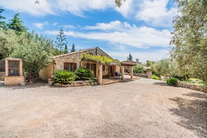 A rustic stone house with a gravel driveway, surrounded by greenery and trees. - Rustic Country Retreat for 4 (Pollença)