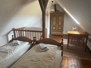 Une chambre avec deux lits simples, une commode en bois, une table et une chaise.