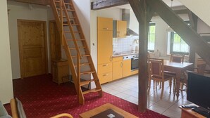 A multi-level living space with a wooden staircase, a dining area with a table and chairs, and a kitchen with yellow cabinets.