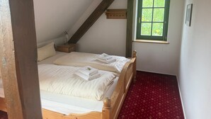 A bedroom with a sloped ceiling, a wooden bed, a nightstand, a window with a view of greenery, and a red carpet.