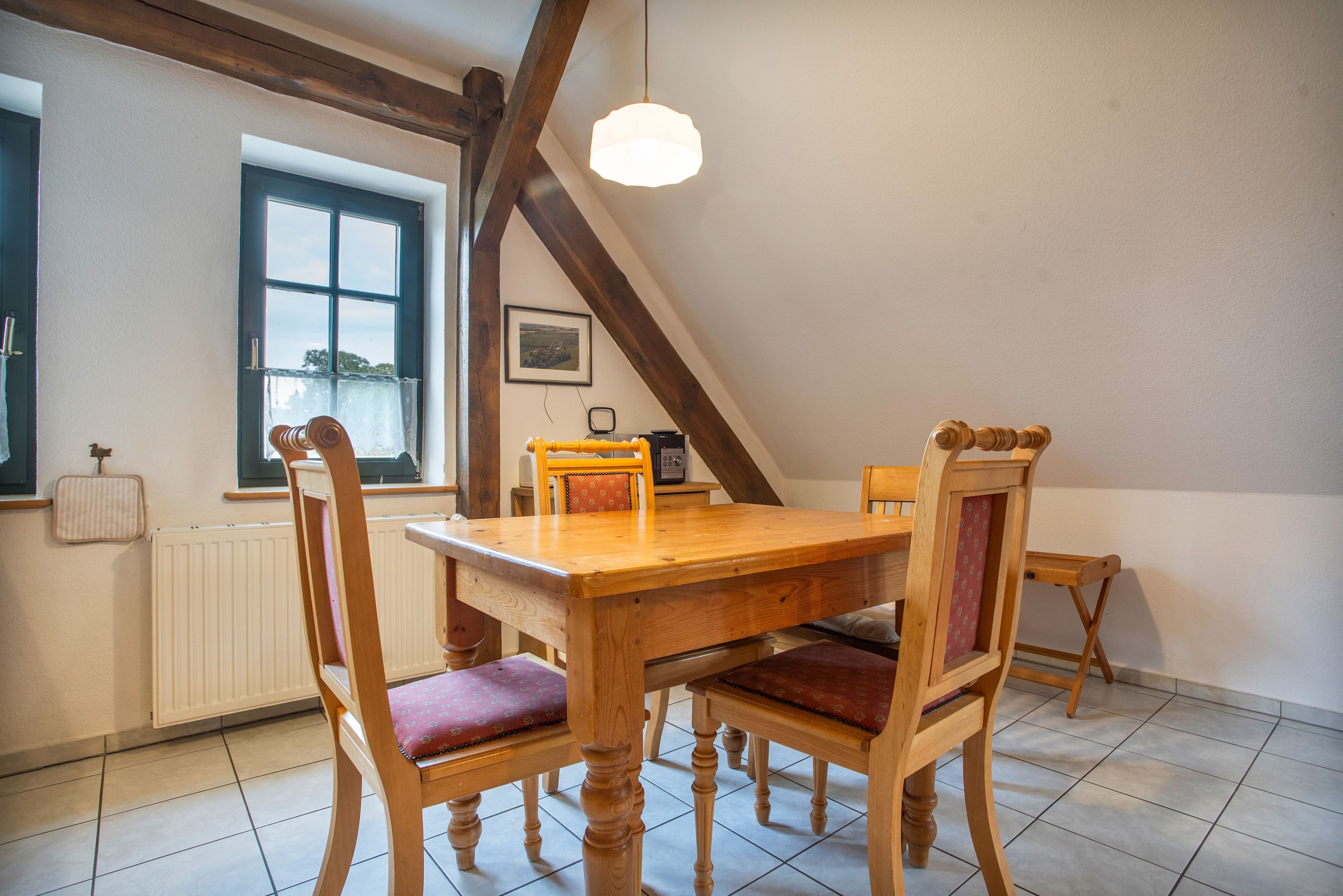 Un comedor con mesa y sillas de madera, una ventana con vistas, y una lámpara colgante.