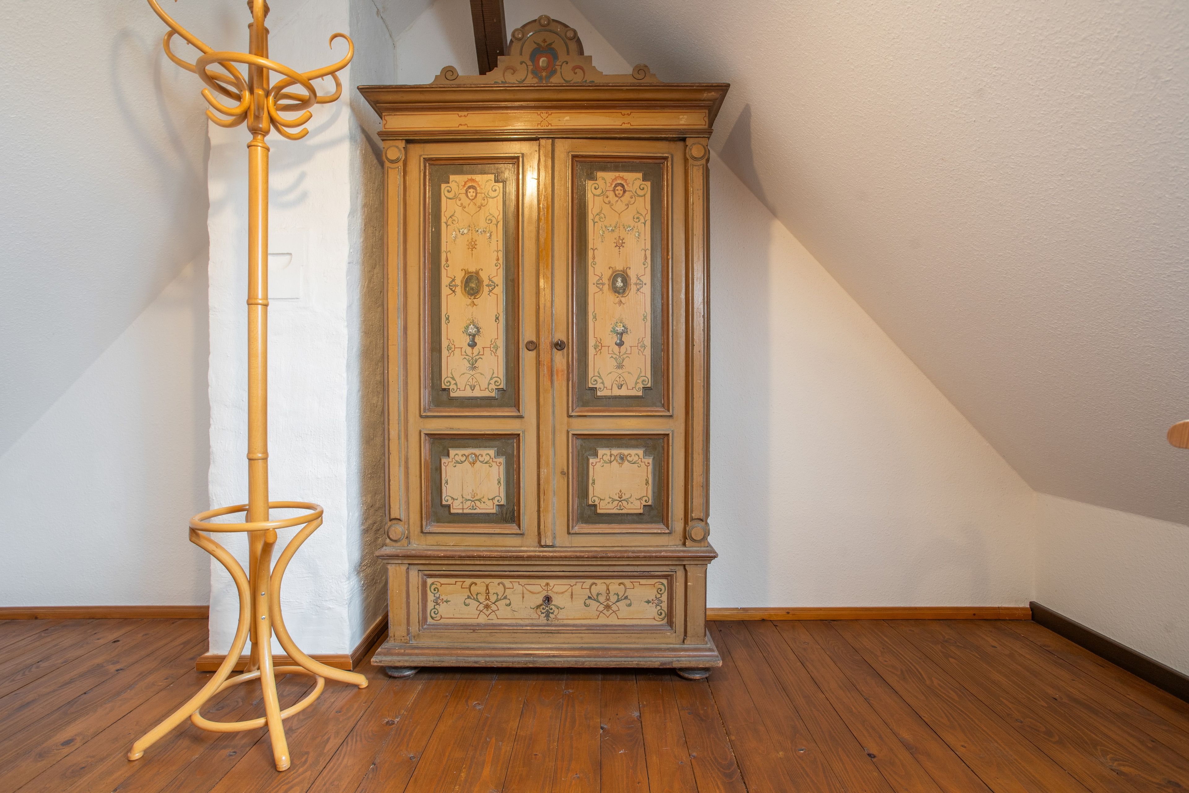 Un plancher en bois, un grand lampadaire et une grande armoire en bois ornée de panneaux décoratifs.