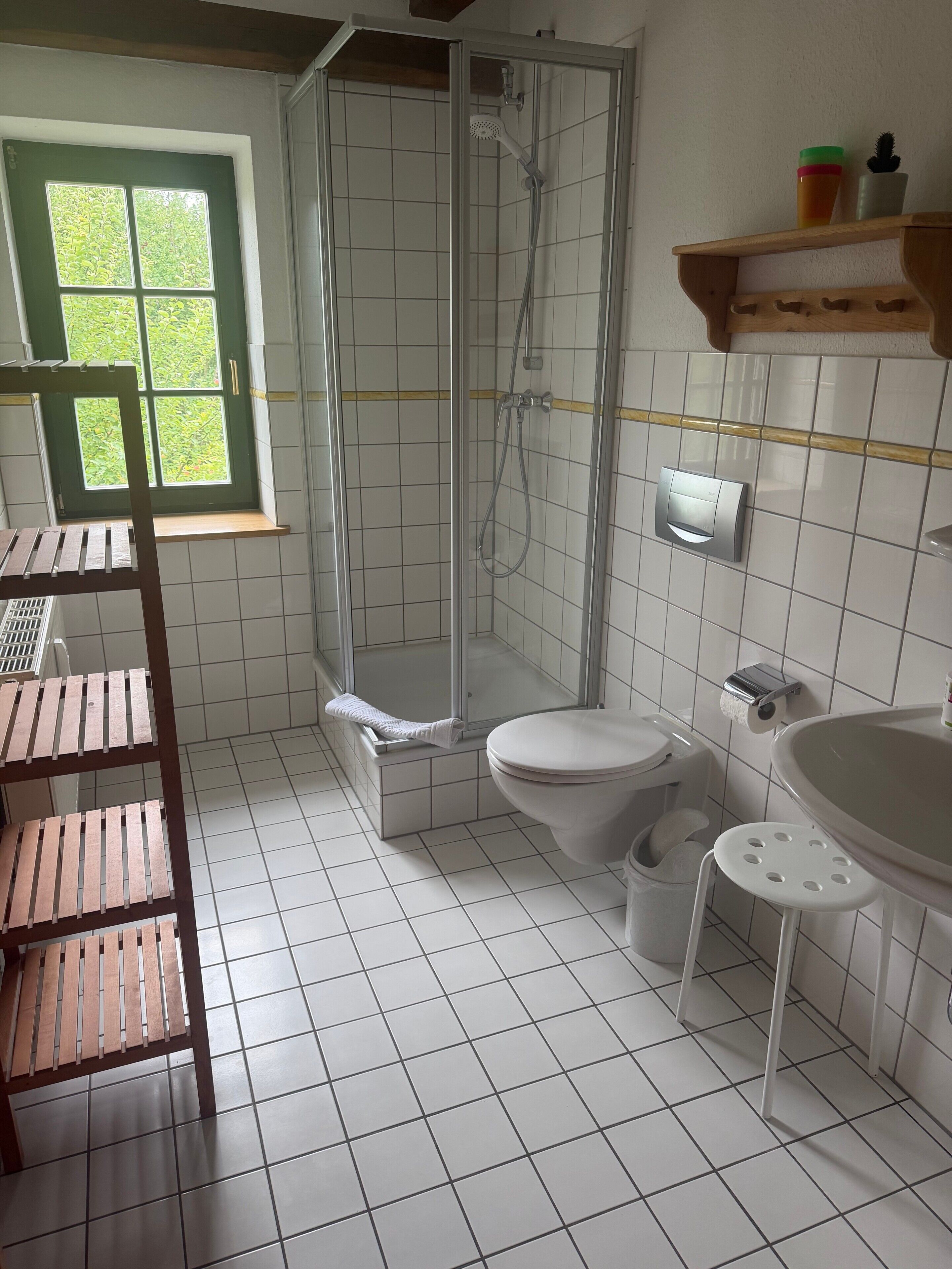 Ein Badezimmer mit Dusche, Toilette, Waschbecken und einem Fenster mit Grünpflanzen draußen.