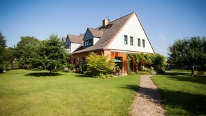 A two-story house with a sloped roof, a visible chimney, and a paved pathway leading to the entrance. - Cozy Holiday Apartment with Garden in Solzow Farmhouse (Südmüritz)