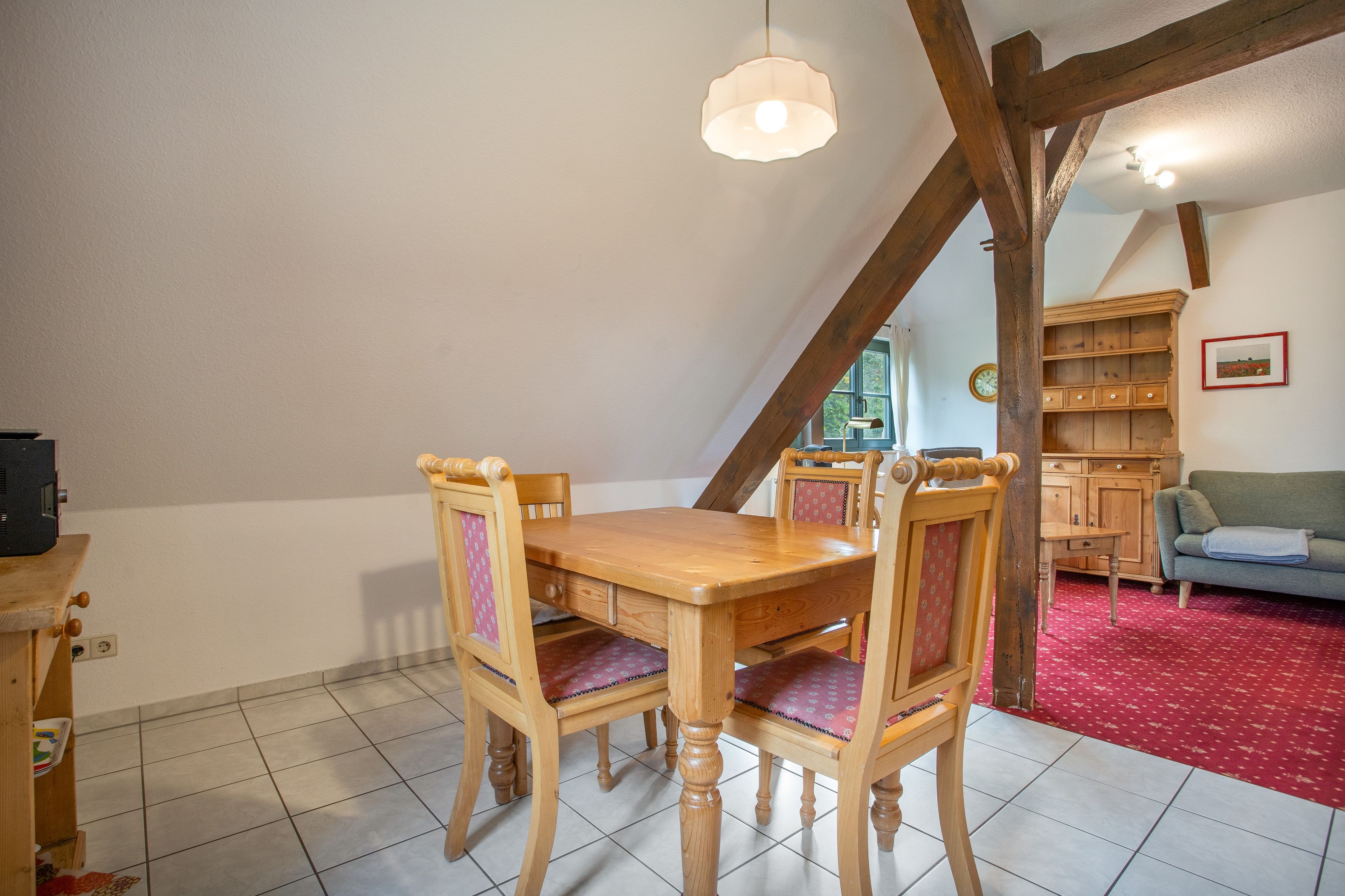A dining area with a wooden table and chairs, a hanging light fixture, and a red carpeted floor.