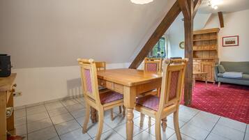 A dining area with a wooden table and chairs, a hanging light fixture, and a red carpeted floor.
