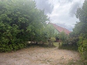 Paisatge rural amb una casa envoltada de vegetació densa i un camí de terra que hi mena.
