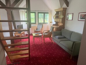 A room with a wooden staircase, a green sofa, a wicker chair, a small table, and a bookshelf.
