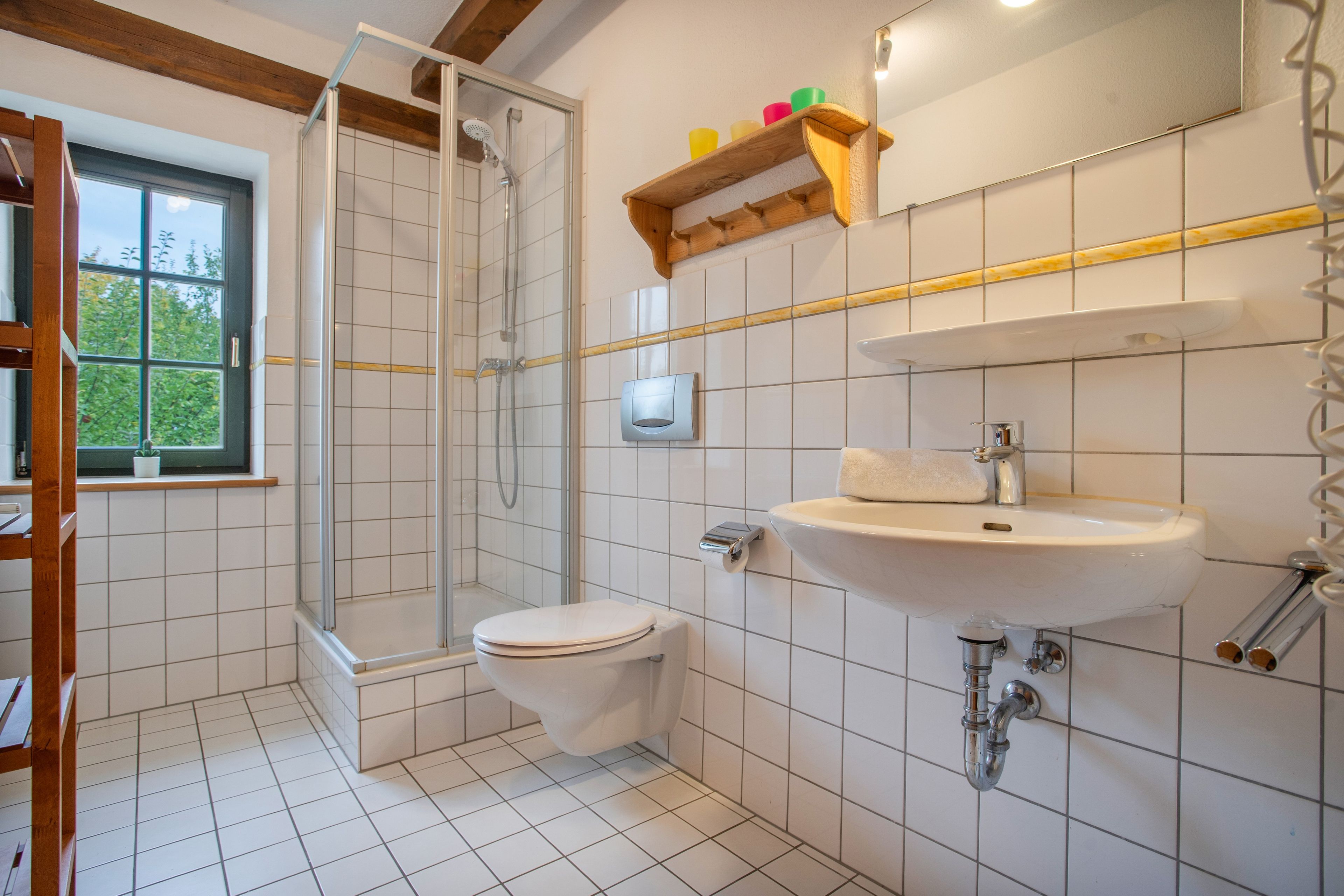 Ein Badezimmer mit Dusche, Toilette, Waschbecken und einem Fenster mit Blick auf Grünflächen.