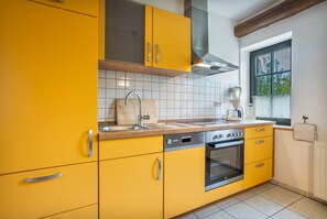 Una cocina con gabinetes amarillos, un lavaplatos de acero inoxidable, un horno empotrado y una ventana con vista a follaje.
