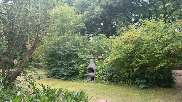 A garden with a barbecue grill and a red folding chair.