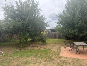 A backyard with a wooden table and chairs, a grassy area, and a wooden fence.