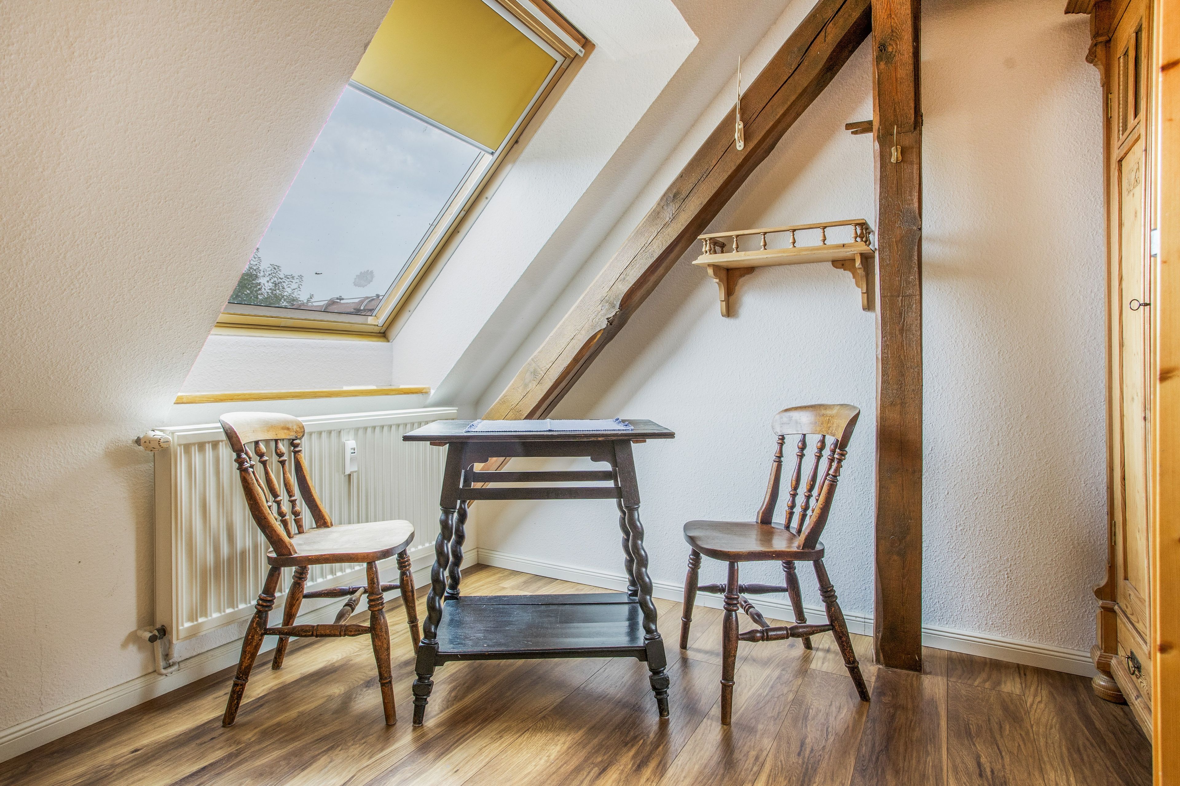Une pièce avec un plafond en pente, une lucarne, une table avec deux chaises et une étagère en bois.