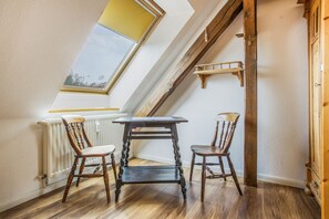 A room with a sloped ceiling, a skylight, a table with two chairs, and a wooden shelf. - Lovely Apartment with Balcony in Solzow Farmhouse (Südmüritz)