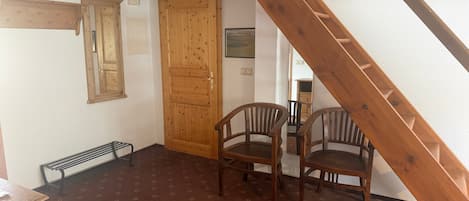 A room with a wooden staircase, a wooden door, two wooden chairs, and a patterned floor.