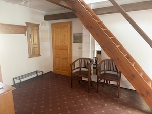 Una habitación con una escalera de madera, una puerta de madera, dos sillas de madera y un suelo con estampado.