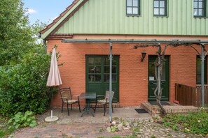 A brick house with a green door, a small patio with a table and chairs, and a pergola with a table umbrella.