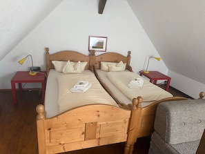 Une chambre avec deux lits simples, une tête de lit en bois, des tables de chevet avec des lampes et un tableau encadré au mur.