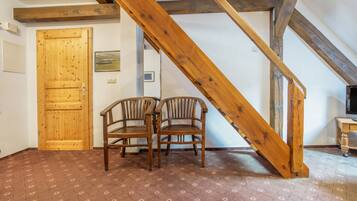 Ein Zimmer mit einer Holztreppe, zwei Holzstühlen, einer Holztür und einem gemusterten Teppich.