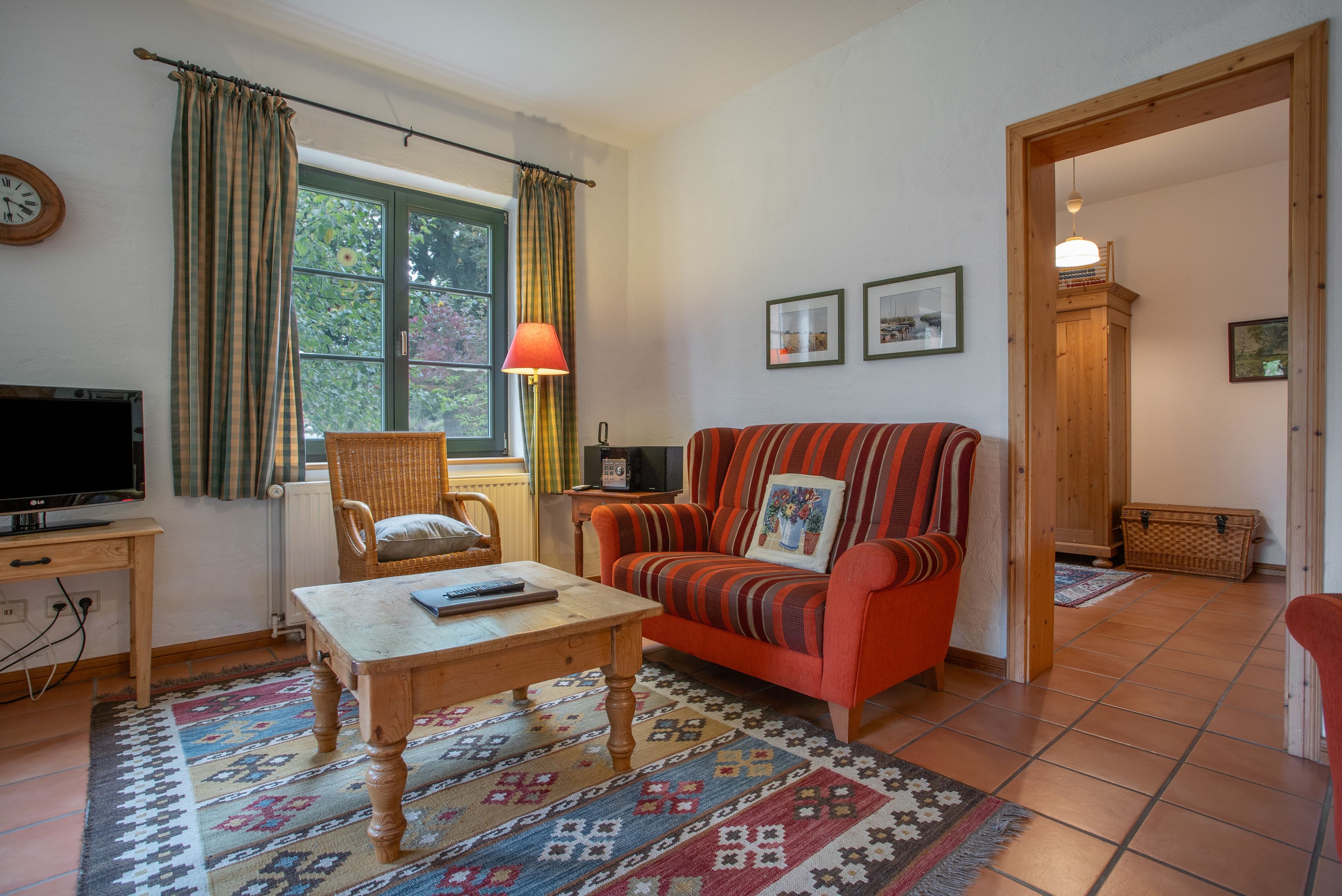 A cozy living room with a television, a wicker chair, a sofa with a patterned cushion, and a patterned rug.