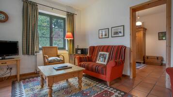 A cozy living room with a television, a wicker chair, a sofa with a patterned cushion, and a patterned rug.