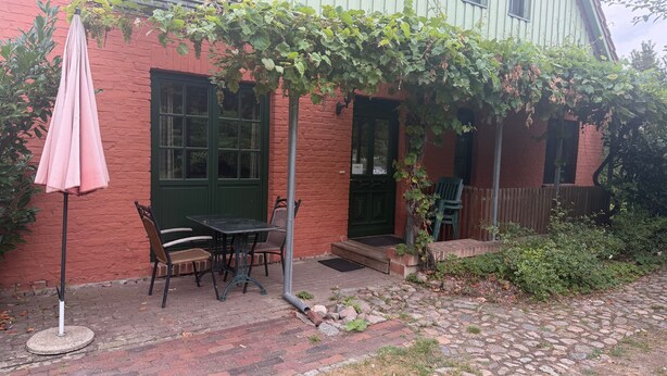 A brick patio with a table and chairs, a green door, and a vine-covered wall. - Apartment '4' with Shared Garden and Wi-Fi (Südmüritz)