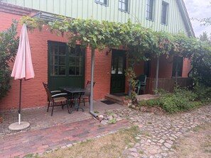 A brick patio with a table and chairs, a green door, and a vine-covered wall.