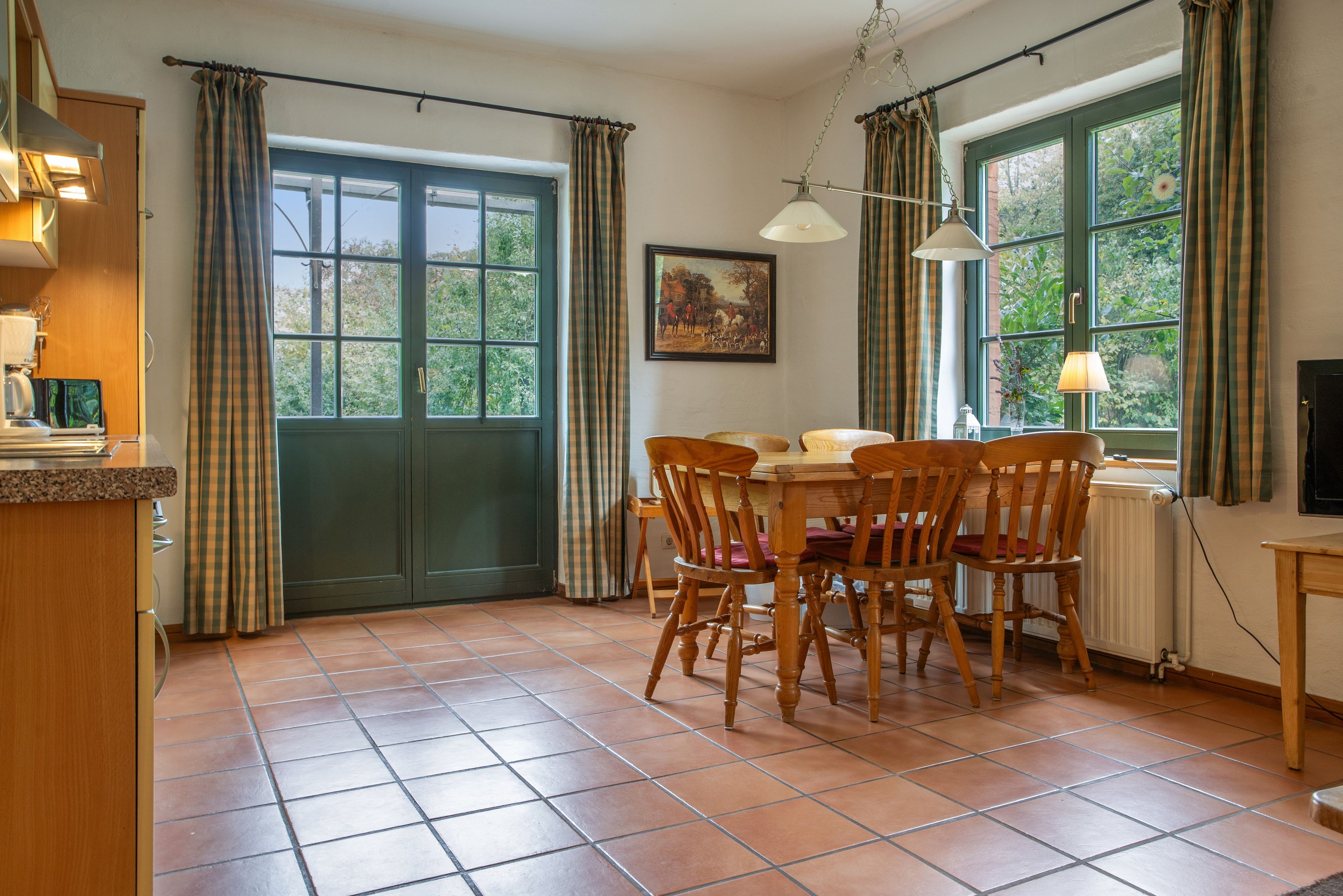 A dining area with a wooden table and chairs, a painting on the wall, and a window with curtains.