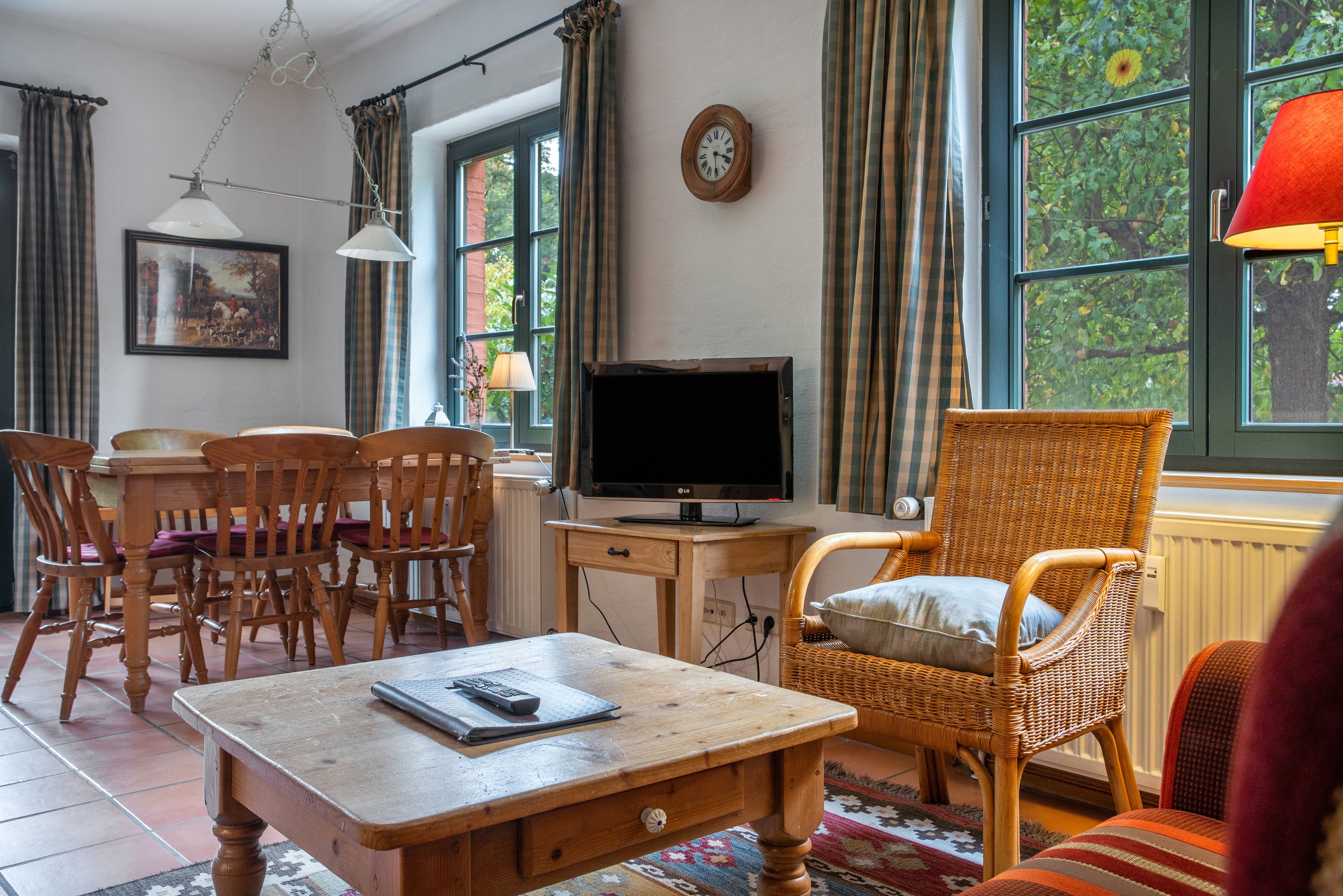 Ein gemütliches Wohnzimmer mit einem Holz-Fernsehschrank, einem Korbstuhl und einem Esstisch mit Stühlen.