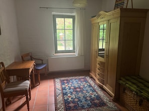 Habitació amb taula de fusta, dues cadires, un armari, finestra que mostra vistes a vegetació i una catifa amb dibuixos.