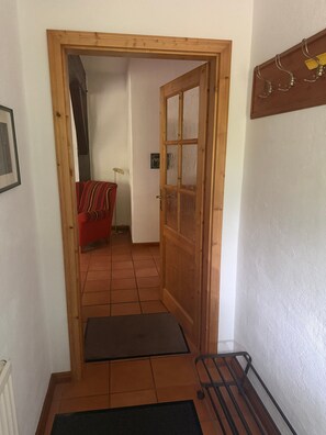 Una puerta de madera que da a una habitación con un sofá rojo y piso de baldosas.
