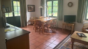 A dining area with a wooden table and chairs, a television on a stand, and a kitchen area with a sink and cabinets. - Apartment '4' with Shared Garden and Wi-Fi (Südmüritz)