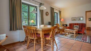 Un coin repas avec une table et des chaises en bois, une fenêtre avec des rideaux, une lampe et un canapé rouge.