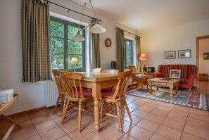 Ein Essbereich mit einem Holztisch und Stühlen, einem Fenster mit Vorhängen, einer Lampe und einem roten Sofa.