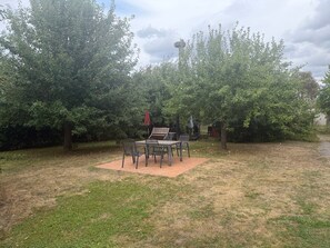 Un espace extérieur aménagé en terrasse, avec une table et des chaises, entouré d’arbres et doté d’un barbecue.