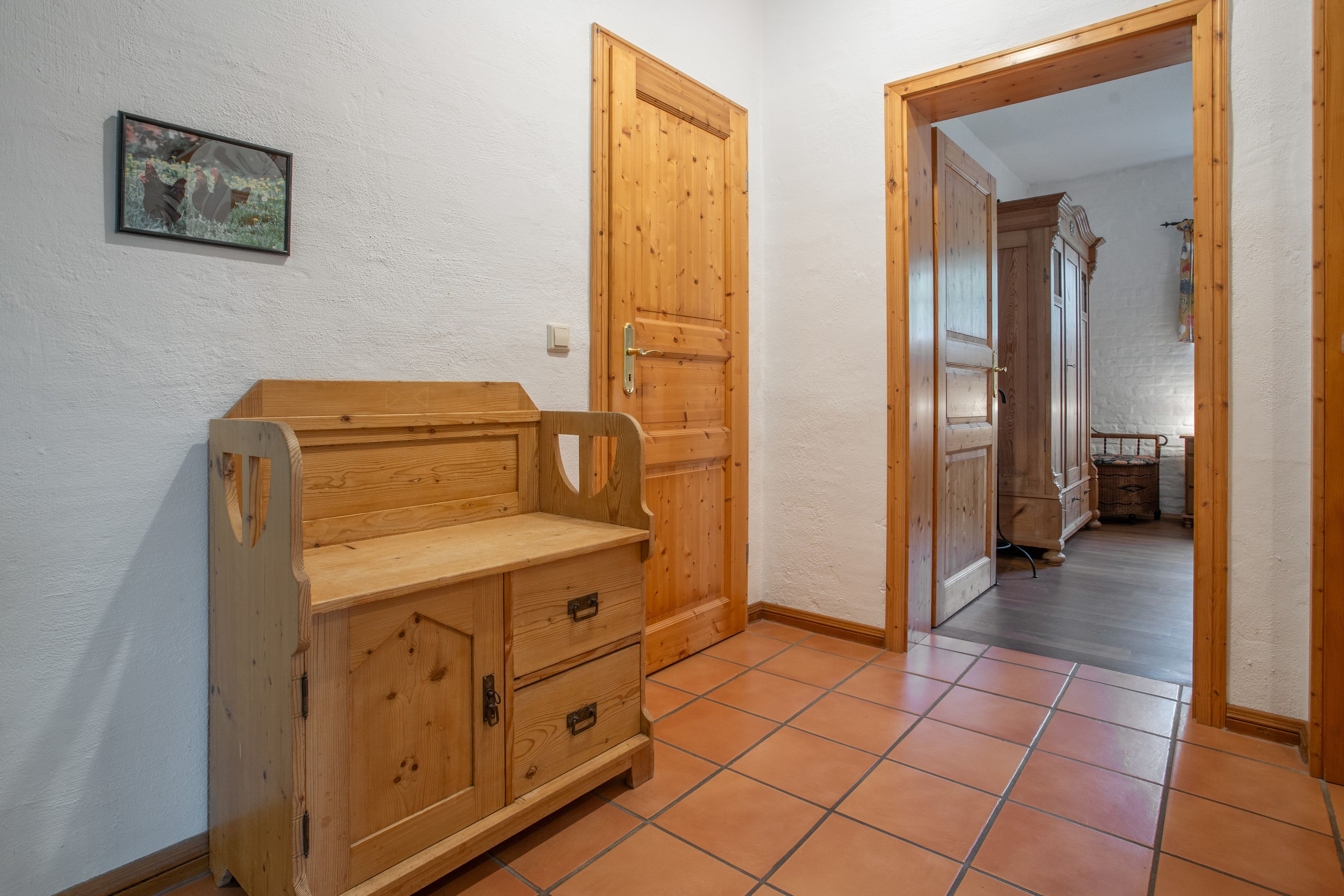 Un couloir meublé de meubles en bois, doté d’un sol carrelé et d’une porte donnant sur une autre pièce.