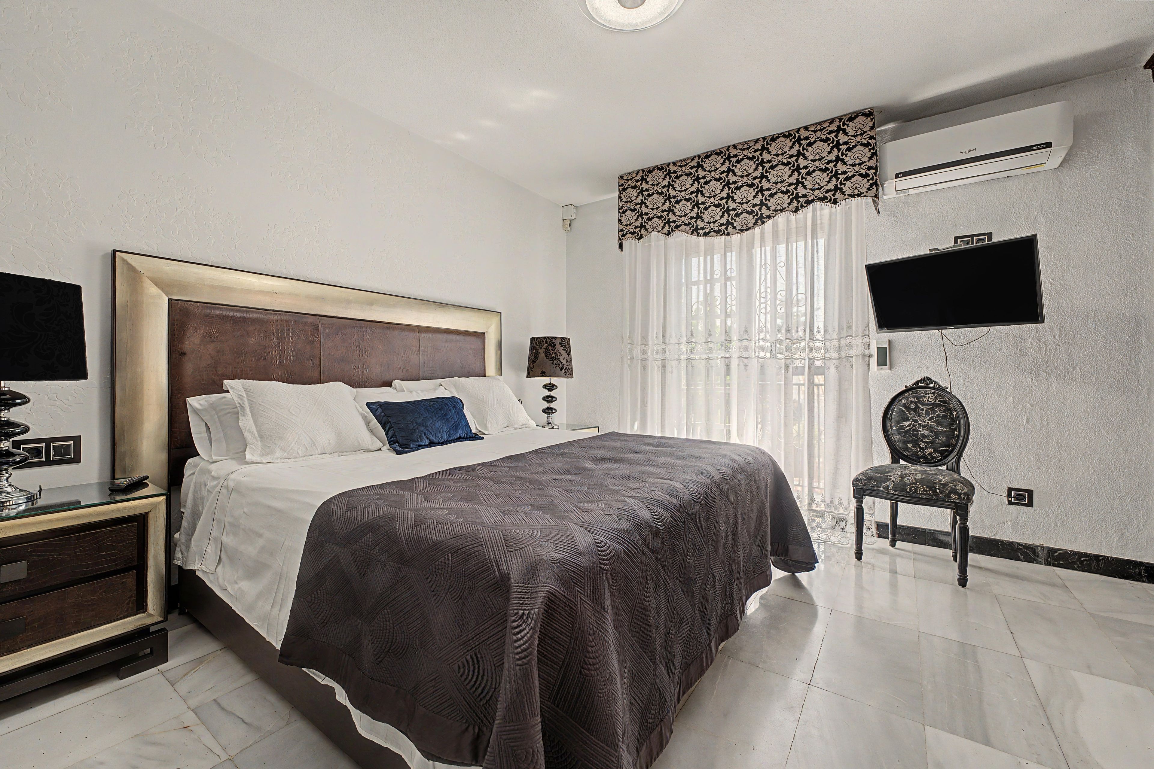 A hotel room with a bed, a nightstand, a chair, a TV, and a window with curtains.