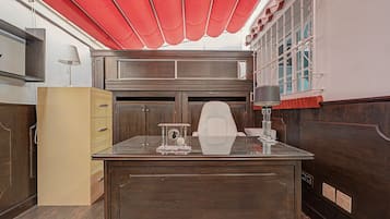 A room with a wooden desk, a lamp, a red awning, and a window with decorative ironwork.