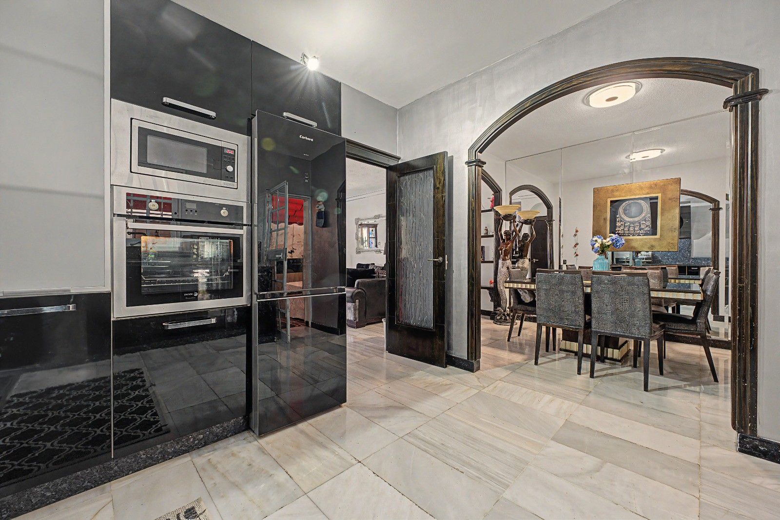 Una cocina moderna con un separador de vidrio, un comedor con mesa y sillas, y vistas al salón.