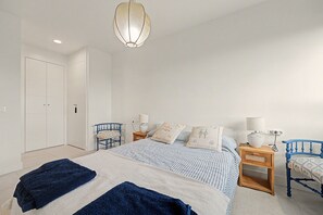 Une chambre à coucher comprenant un lit, deux tables de chevet, une chaise, une armoire et un luminaire suspendu.
