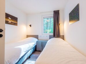 Ein Doppelzimmer mit zwei Betten, einem Fenster mit Blick auf Bäume, einem Schreibtisch und einem Schrank.
